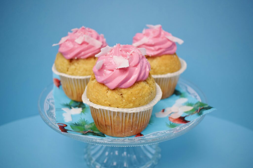 Three homemade cupcakes with pink frosting on a glass stand, perfect for dessert and parties.